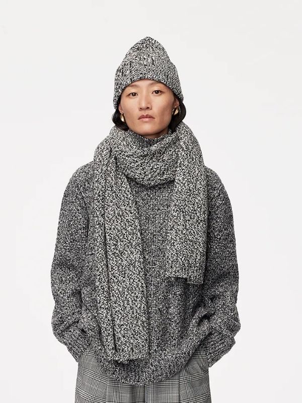 Woman wearing a thick gray speckled scarf, matching hat, and oversized sweater from Another Tomorrow, styled with plaid trousers for a luxury winter look