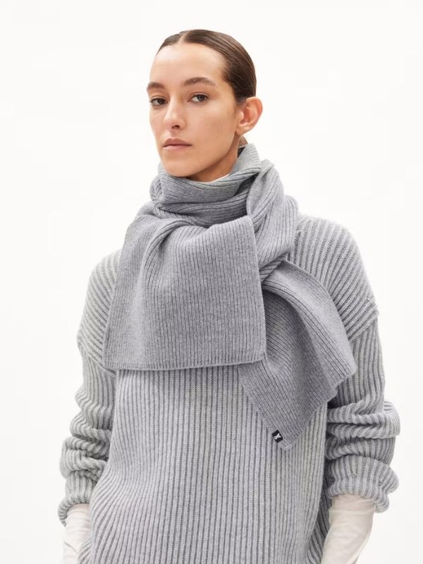 Woman wearing a chunky light gray knit scarf and matching sweater from ARMEDANGELS, styled for a cozy minimalist winter look