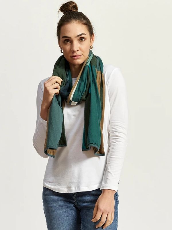 Woman wearing a color-blocked green, tan, and black upcycled scarf from Citizen Wolf, styled with a white long-sleeve shirt and jeans