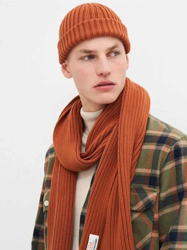 Man wearing an orange ribbed knit scarf and matching beanie from Kuyichi, styled with a flannel shirt and turtleneck