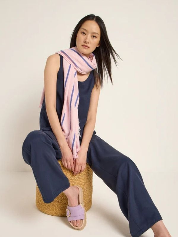 Woman sitting on a stool wearing a soft pink and purple striped scarf from LANIUS, paired with a navy jumpsuit and lilac sandals for a modern spring look