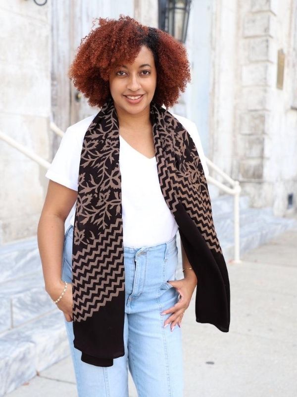 Woman wearing a black and brown fair trade scarf from Passion Lilie, standing outdoors in casual sustainable fashion outfit.
